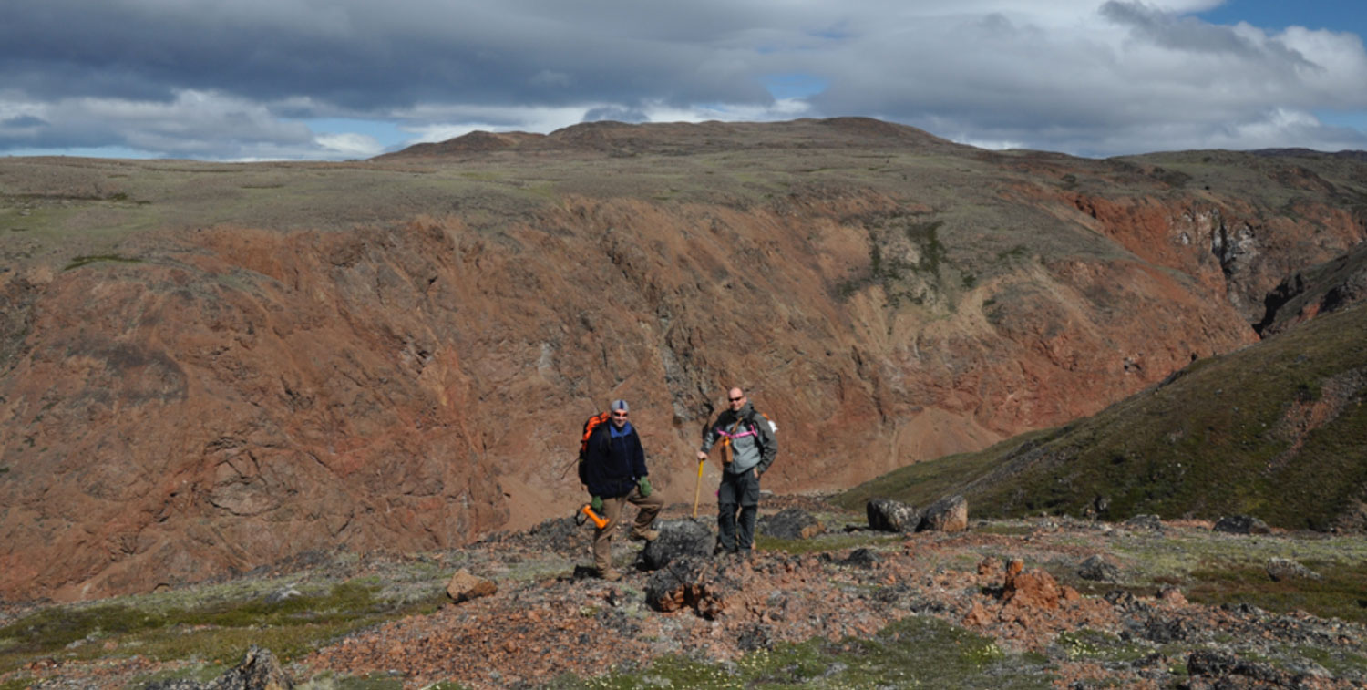 Two geologists on a ridge above the red-brown carbonatite of the Sarfartoq valley